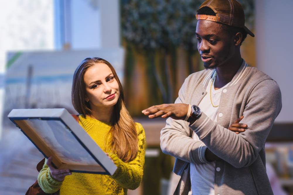 Een Afrikaans uitziende man en Europees ogende dame bekijken samen een kunst werk terwijl ze er over praten