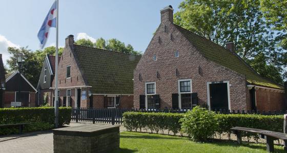 Kleine vissershuisjes van baksteen met witte kozijnen en groene luiken. De hekjes voor het huis komen uit op het met heg omheinde grasveld