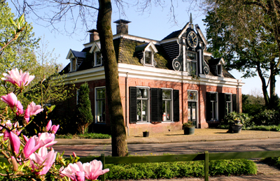 Het museumpand op een zonnige dag, met roze bloemen en een groen grasveld op de voorgrond