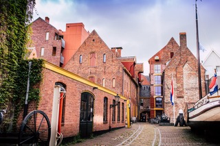 Een straat met bakstenen gebouwen en op de kade een schip.