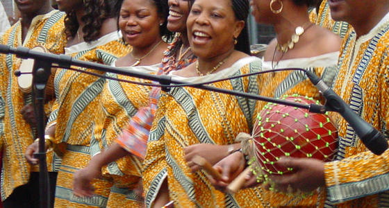 Afrikaanse vrouwen in gele traditionele jurken zingend achter een microfoon