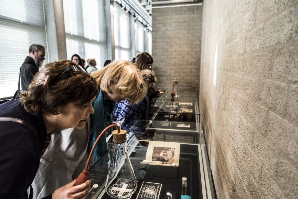 mensen buigen zich over vitrines waar parfumflessen op staan om geuren te kunnen ruiken die bij de attributen in de vitrine passen.