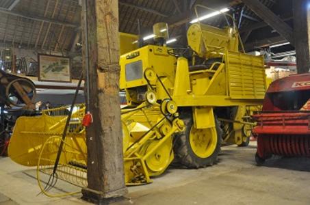 In een grote hoge houten schuur staat een grote gele landbouwmachine