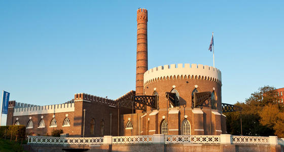 Het museum met roodstenen muren en witte kantelen in de ondergaande zon. Het gebouw kenmerkt zich door zijn ronde toren en hoge schoorsteen.