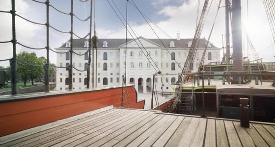 Vanaf een boot is tussen het tuig van de zeilen en de klimtouwen door het museum te zien. Een groot wit statig gebouw