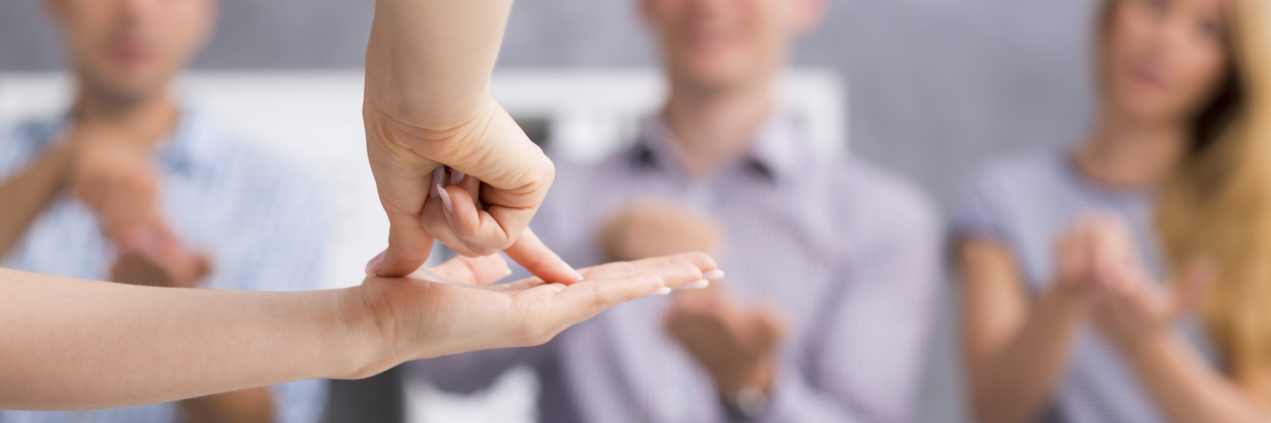 Een foto met op de voorgrond een platte linkerhand met daarop de duim en wijsvinger van de rechterhand die een tentje vormen op de platte hand