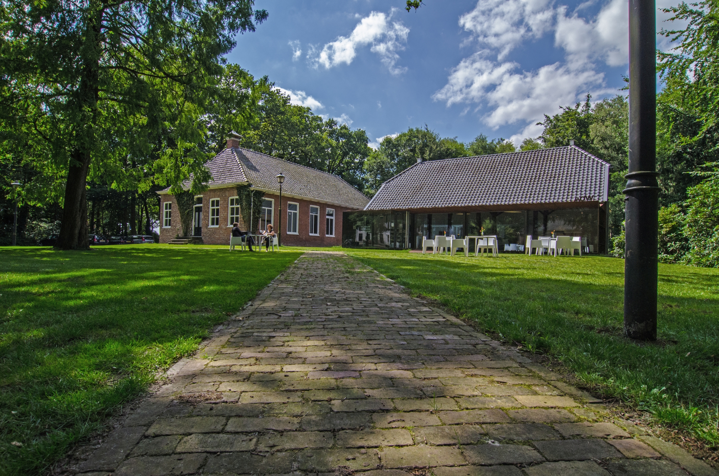 Midden in de natuur tussen de bomen en een groen grasveld ligt aan het eind van een klinkerweg een imposante boerderij waar het museum in is gevestigd.