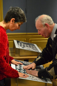 Een man voelt onder begeleiding van een vrouw aan een voelplaat van een tekening van Escher. De tekening is deels in reliëf aangebracht om de techniek uit de kunnen leggen