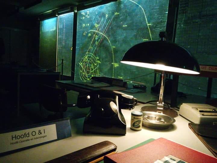 Een bureau met een oude bakelieten telefoon en boeken. Het bureau is schaars verlicht door een enkele bureaulamp