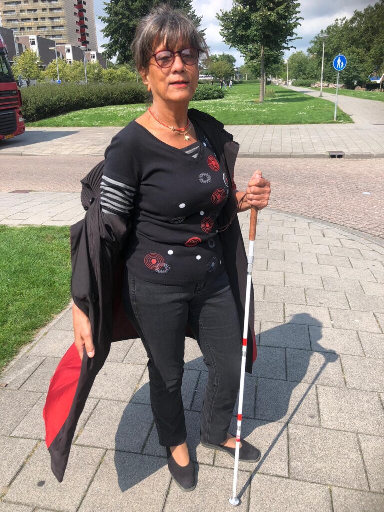 Joan is in het zwart gekleed en heeft haar rode jas nonchalant open geslagen.