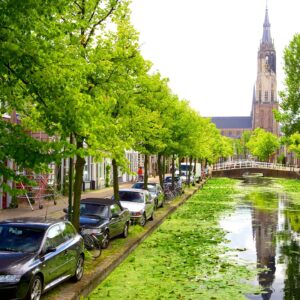 een foto van een van de grachten van Delft met op de achtergrond een kerktoren.