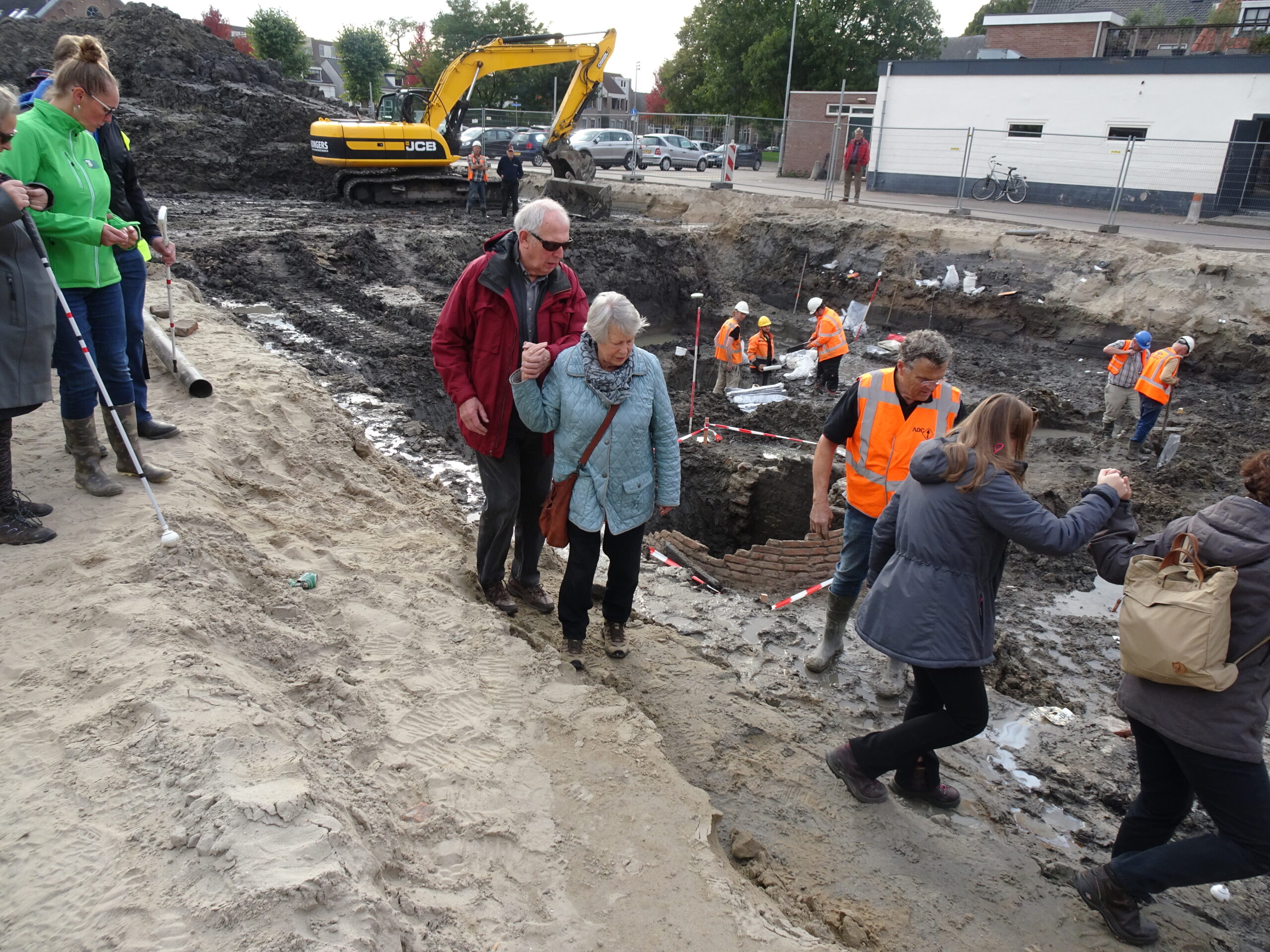 Deelnemers op de rand van de put met de werkende archeologen op de achtergrond
