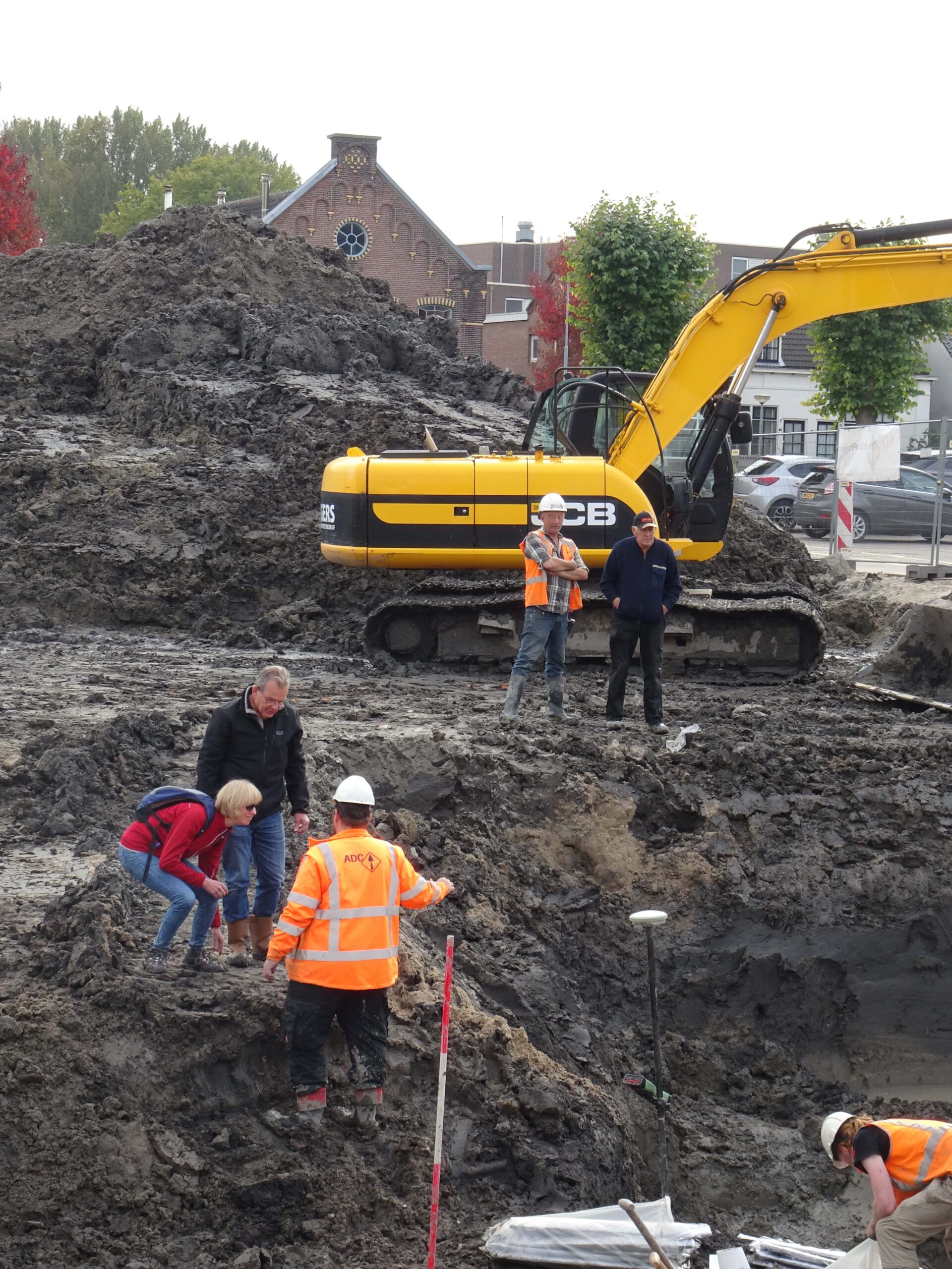 Twee deelnemers aan de rand van de put in gesprek met een van de archeologen.