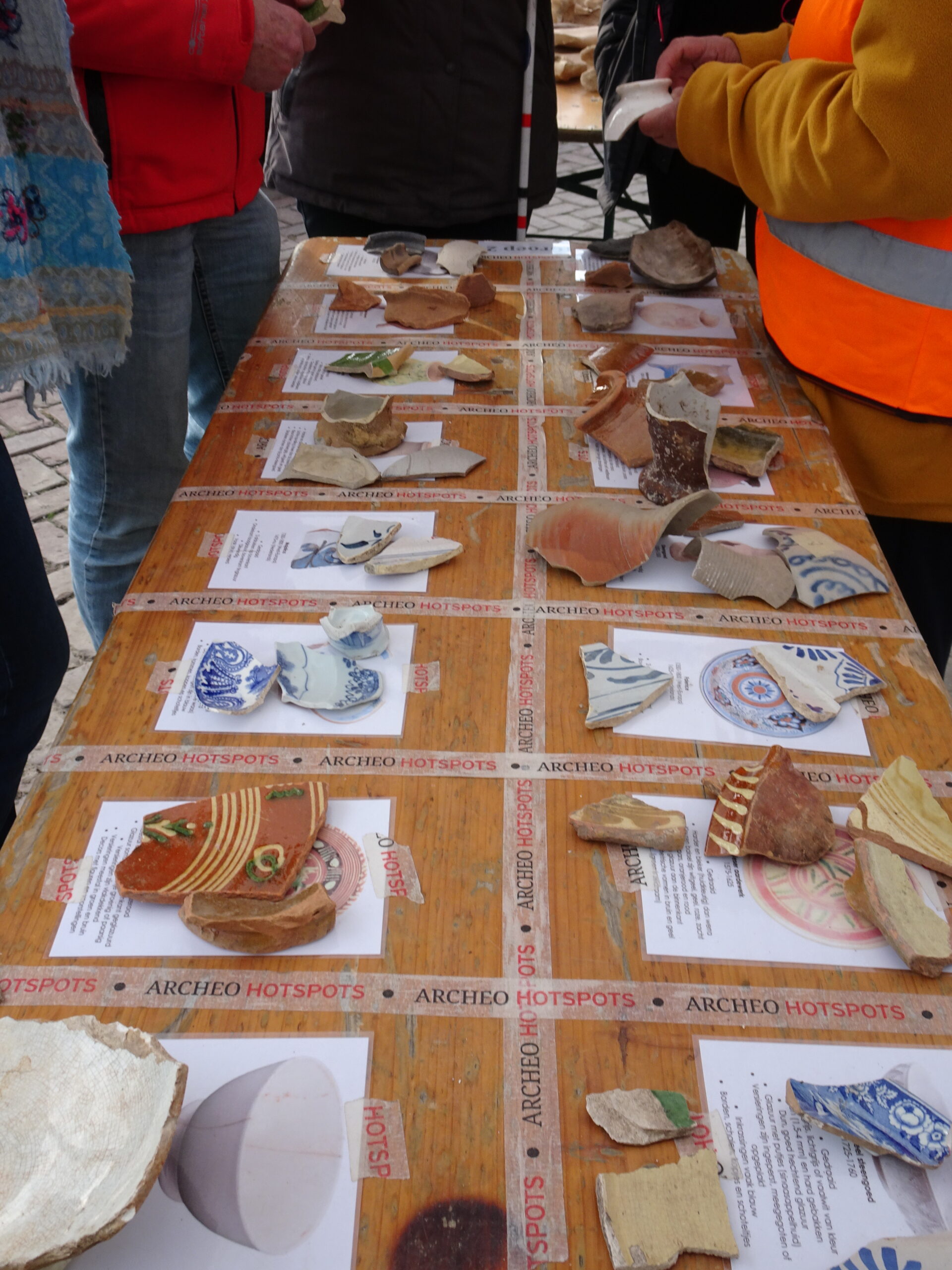 Een tafel vol met scherven van potten met daarbij een afbeelding van het hele object