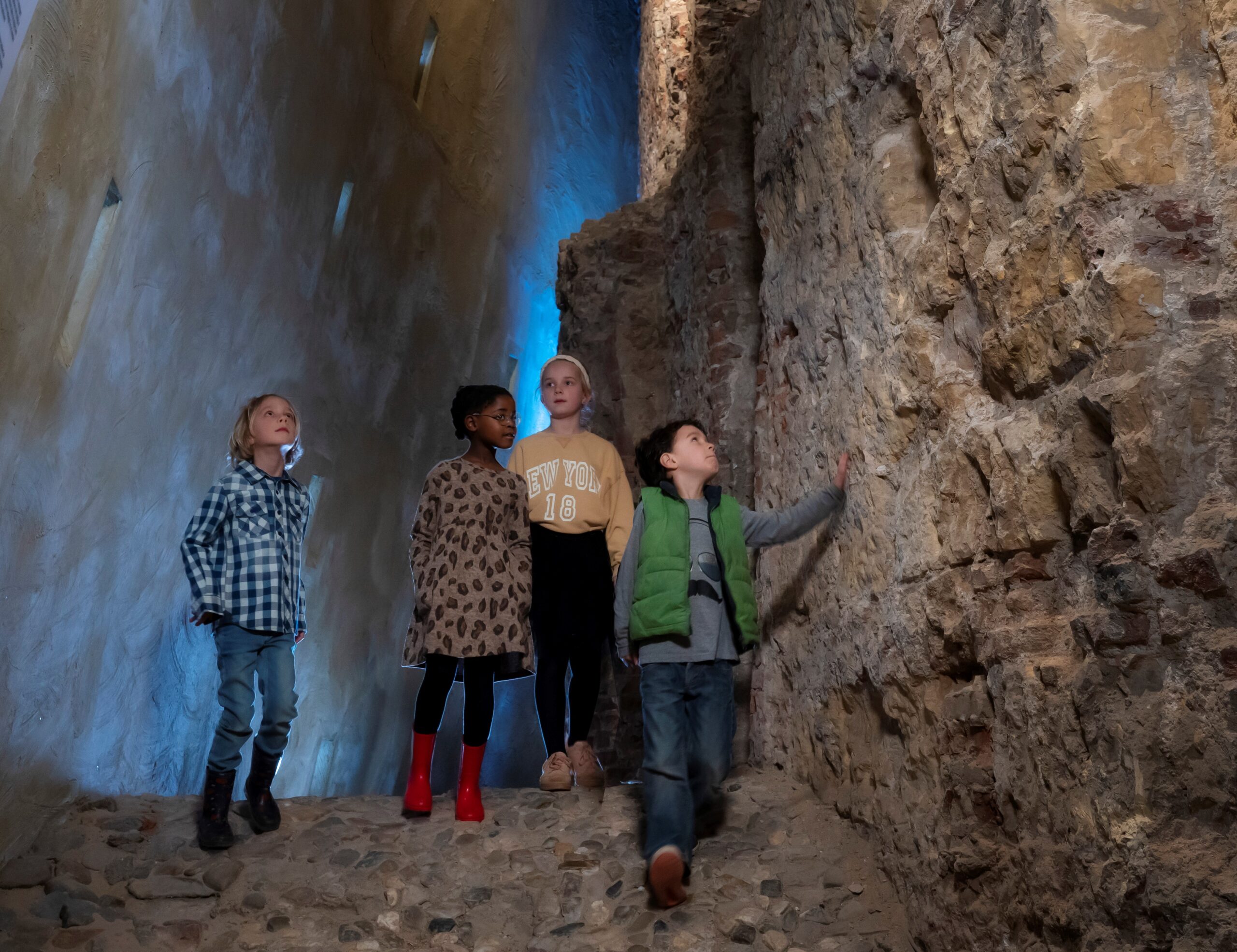 Kinderen lopen door een smalle ruimte met hoge ruw stenen muren